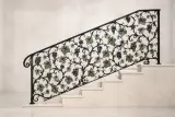 Boczny widok kutej balustrady schodowej na neutralnym tle, prezentujący kąt nachylenia oraz kunsztowne łączenia stalowych pędów.